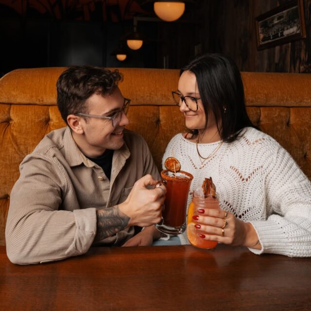 Couple souriant dans une ambiance rétro chez La Belle et La Bœuf, trinquant avec des cocktails gourmands en mode détente.
