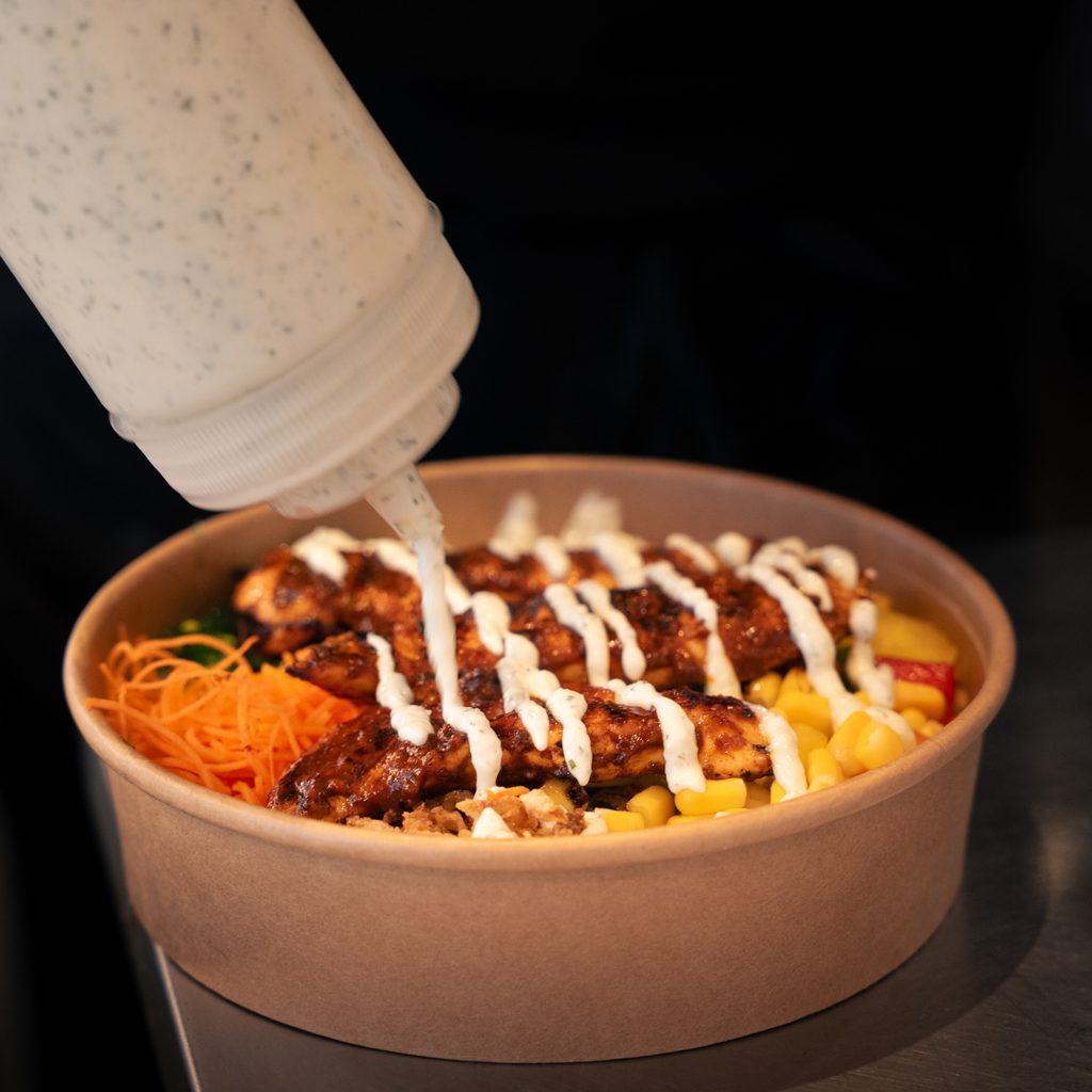 Un bol repas appétissant du restaurant Bol de Vie avec du poulet grillé, des légumes frais et une sauce crémeuse. 