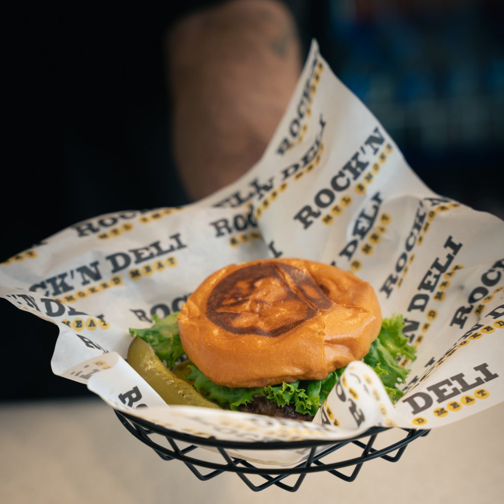 Gros plan appétissant d'un hamburger servi dans un panier avec du papier de marque Rock'n Deli.