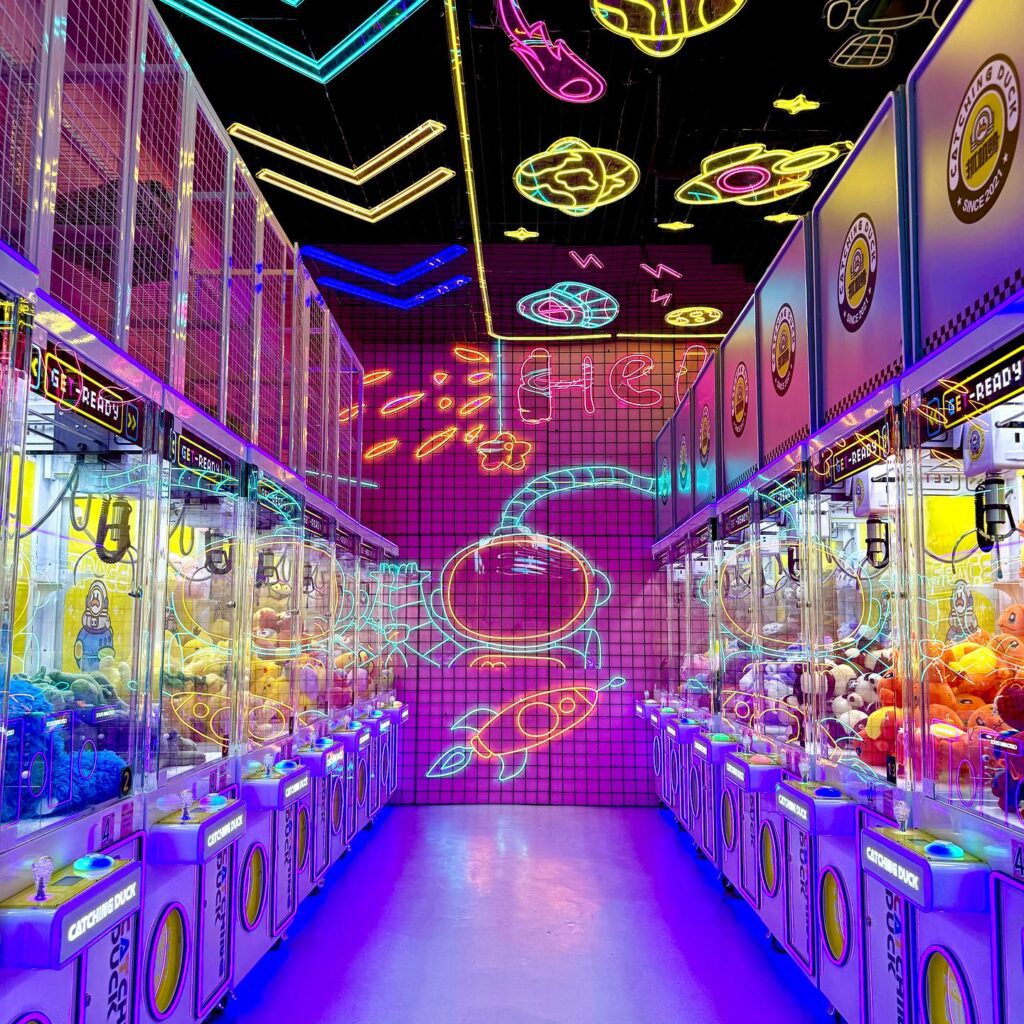 Salle d'arcade vibrante avec des machines à pinces illuminées par des néons colorés.