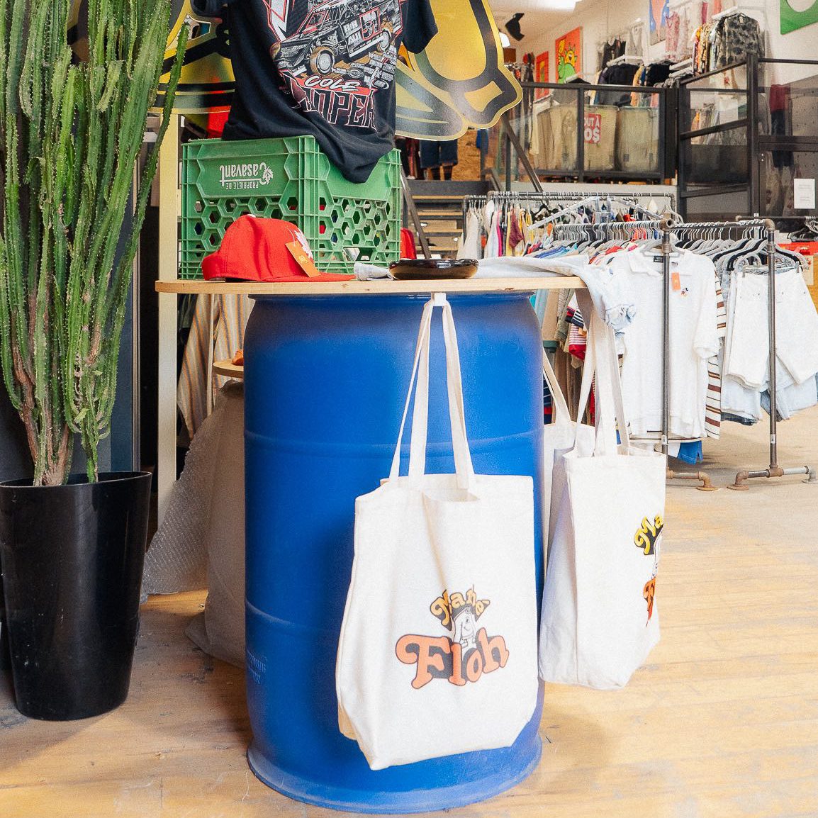 Une vue intérieure de la boutique Marché Floh, montrant des sacs réutilisables avec le logo Floh et des vêtements vintage exposés.