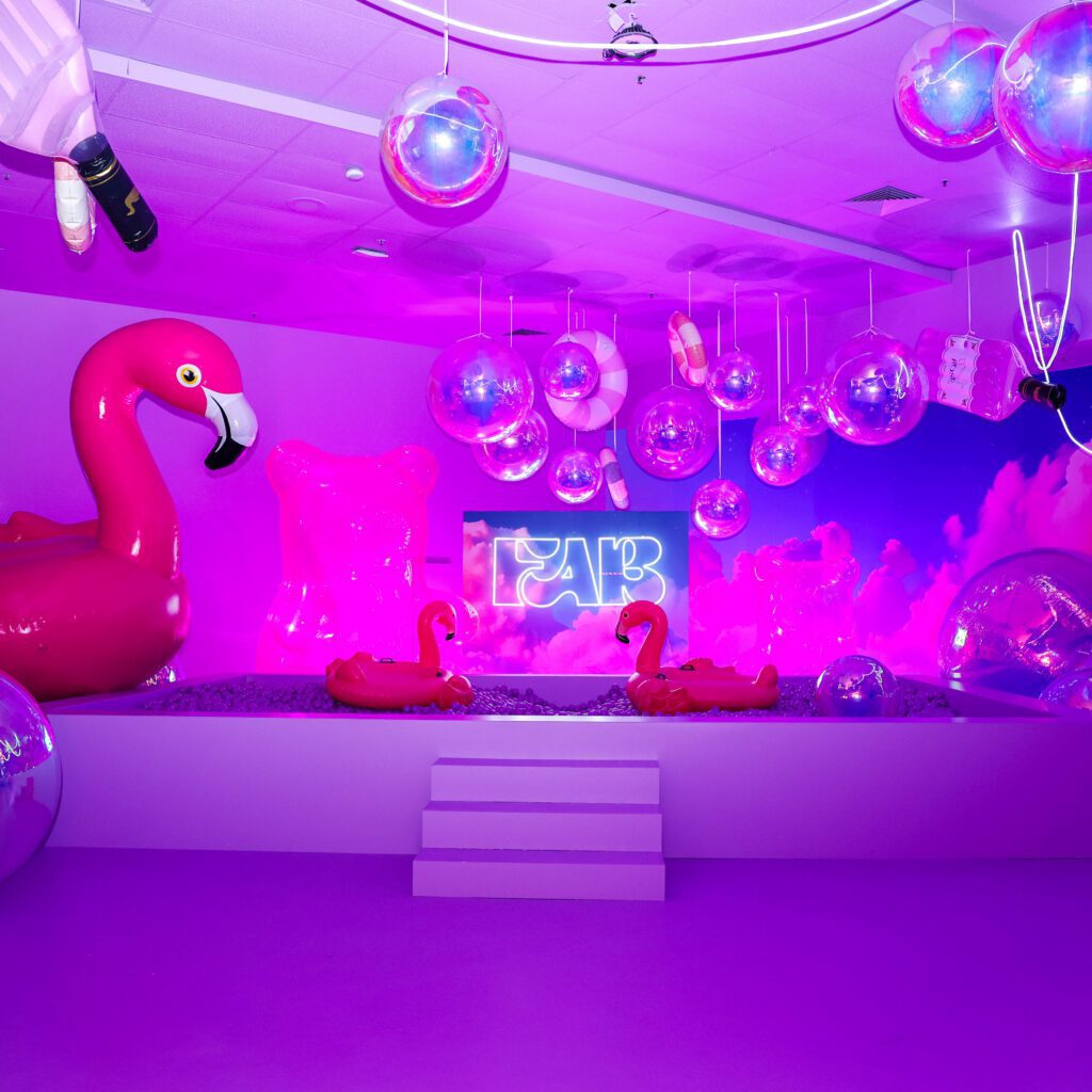 Une installation artistique immersive de l'exposition FAB, avec des flamants roses géants, des boules disco suspendues et un décor rose et violet.