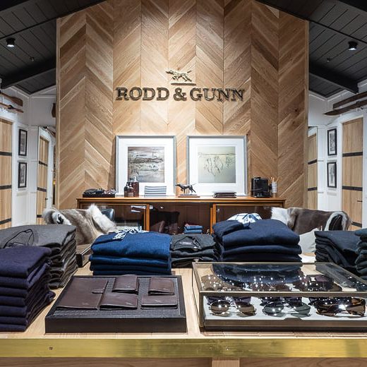 L'intérieur d'une boutique Rodd & Gunn, avec des pulls pour hommes soigneusement pliés sur une table en bois et un logo de la marque sur un mur en bois chevronné.