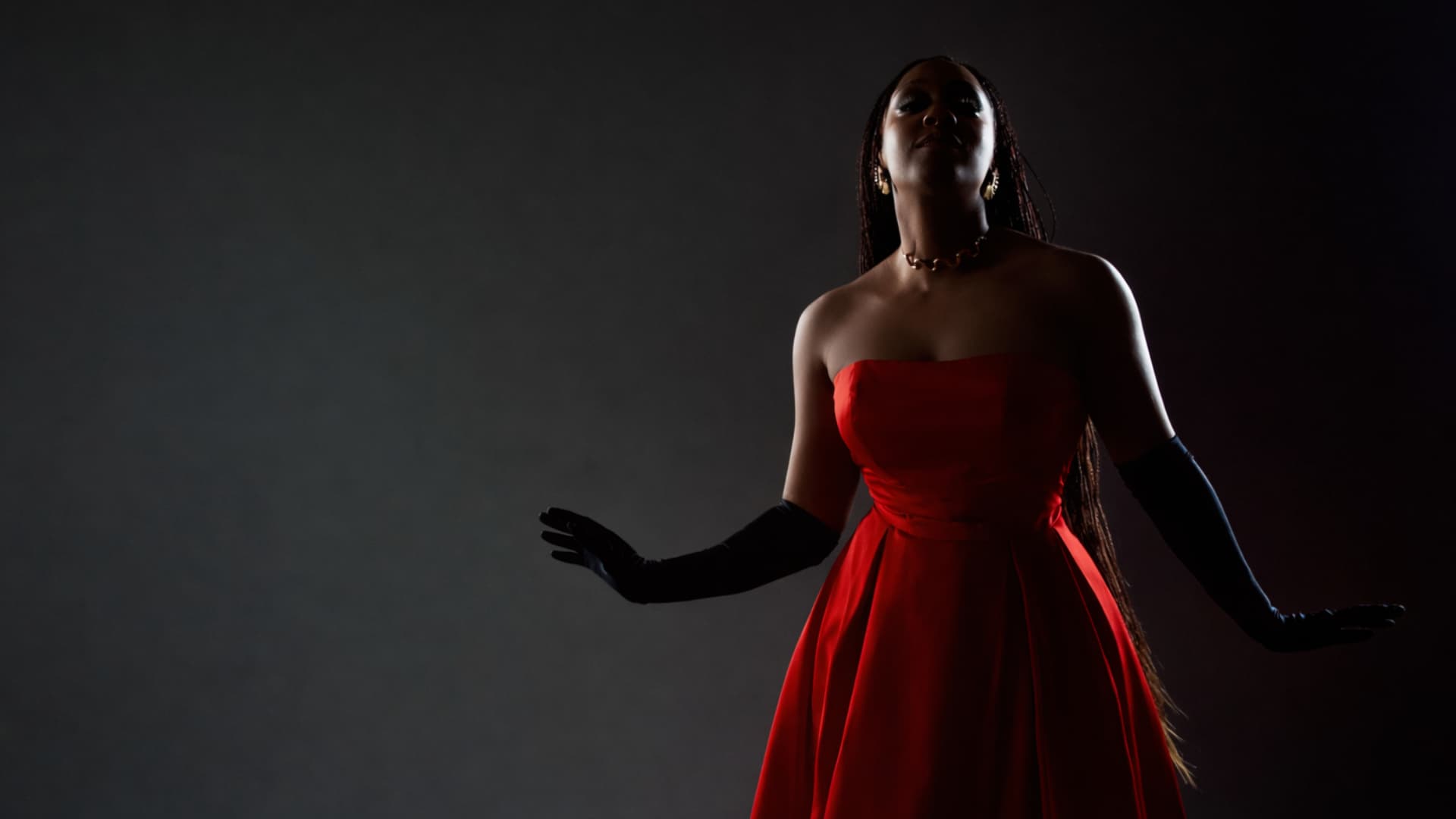 Pamela King portant une robe bustier rouge, devant un fond gris foncé