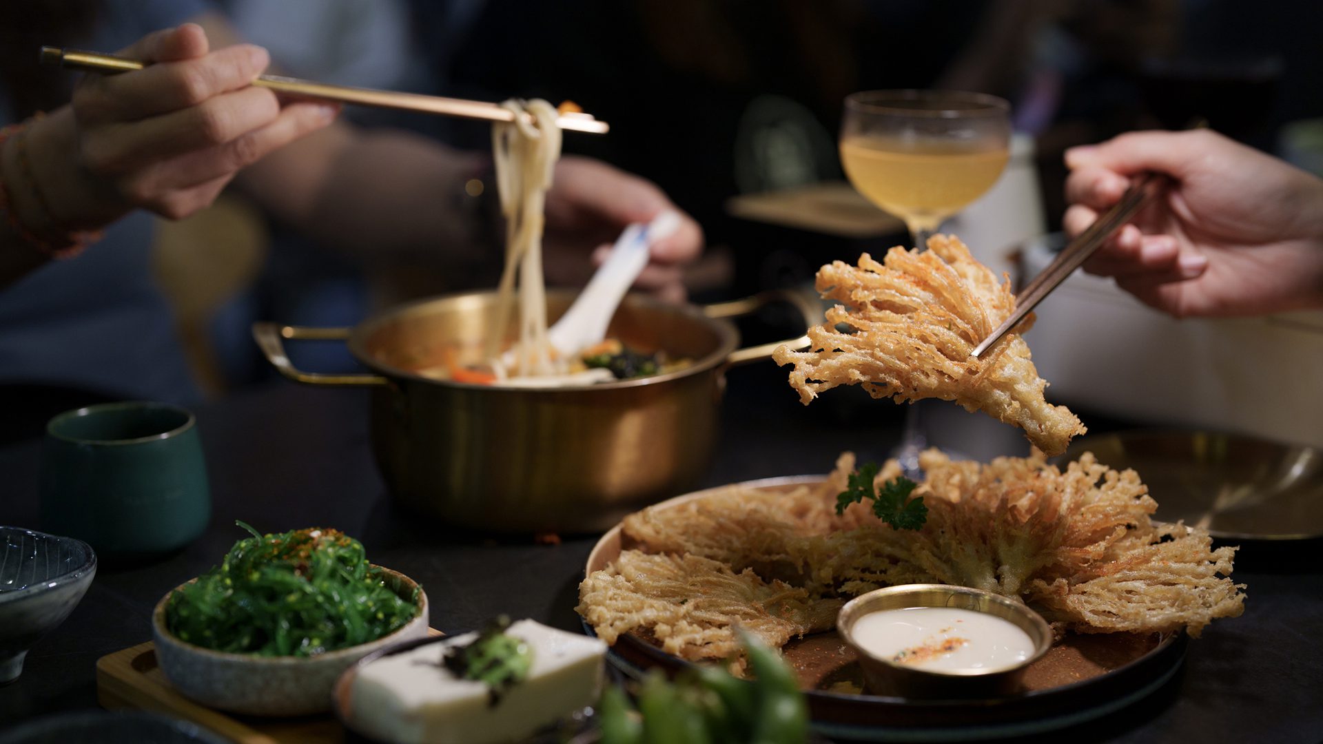 Personnes partageant un bol de ramen japonais avec des baguettes dans un restaurant.