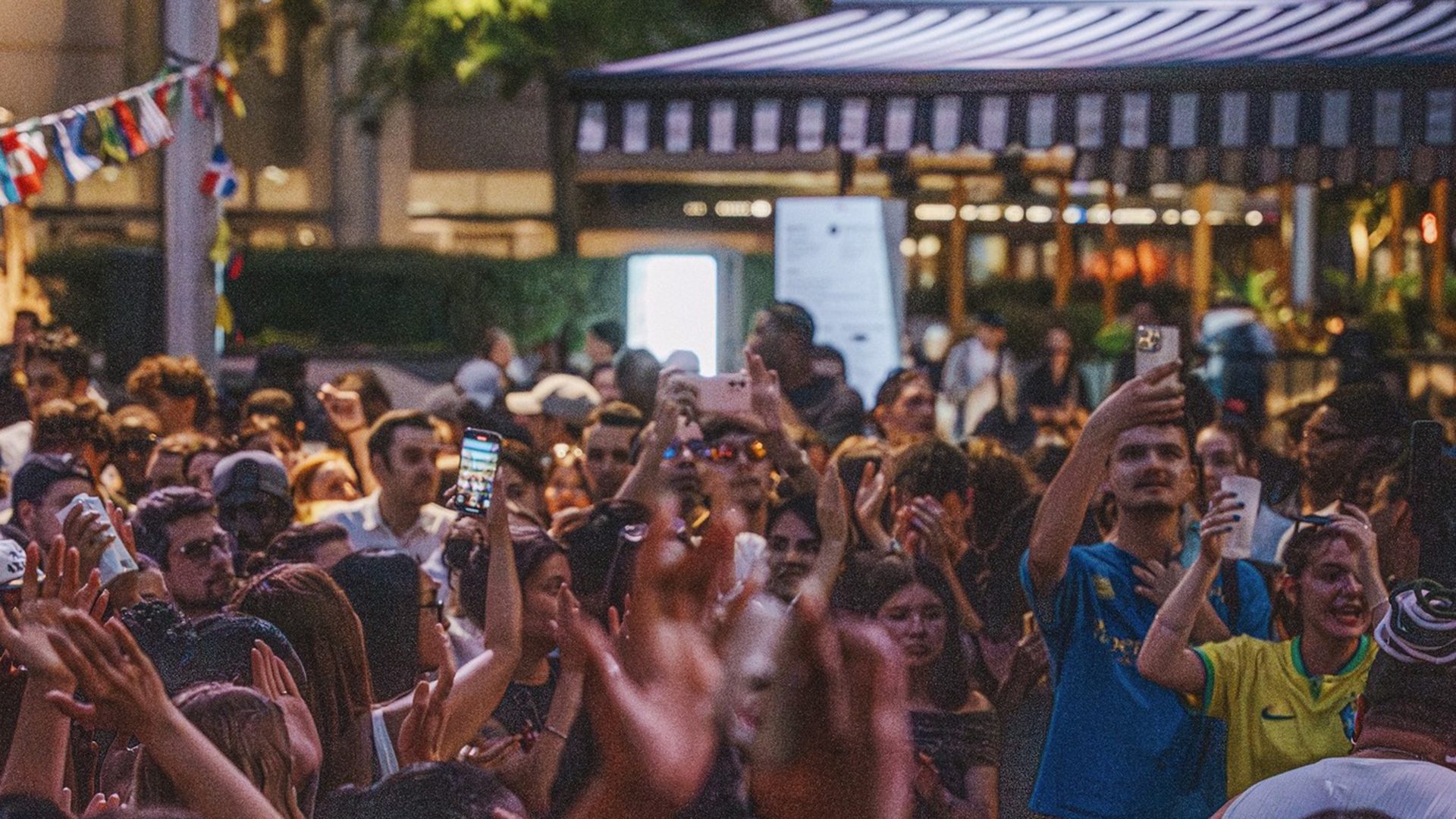 Foule réunie en soirée sous l’Anneau, plusieurs personnes filmant et célébrant dans une ambiance festive.