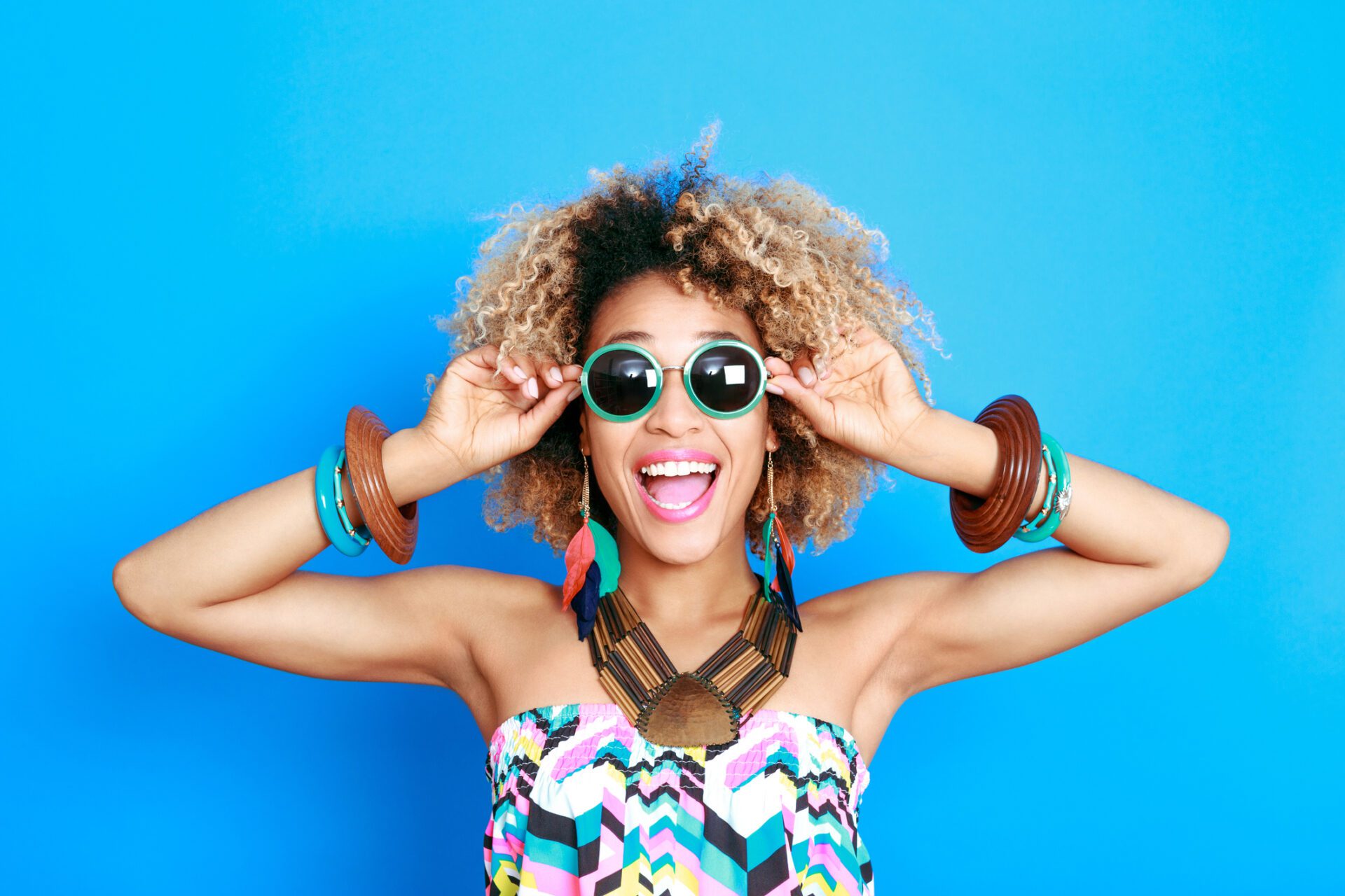 Femme souriante portant des lunettes colorées sur fond bleu.