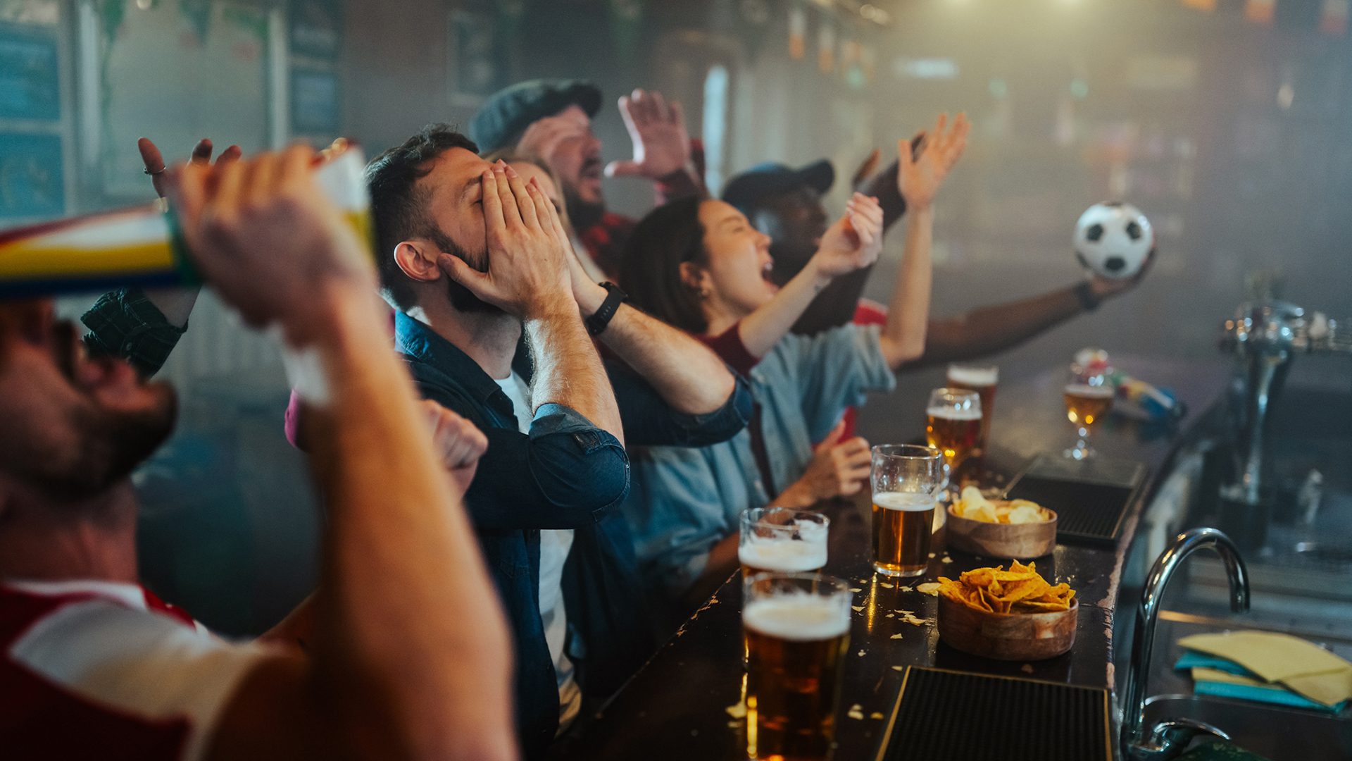 Partisans réunis dans un bar regardant un match de soccer et célébrant une action devant l’écran.