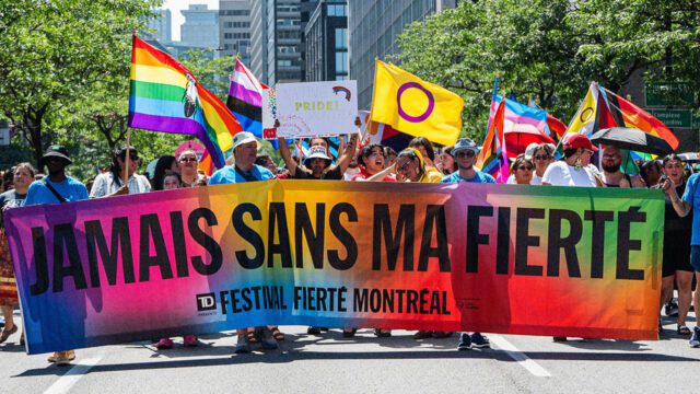 Défilé de la Fierté Montréal avec des participants brandissant des drapeaux arc-en-ciel dans le centre-ville.